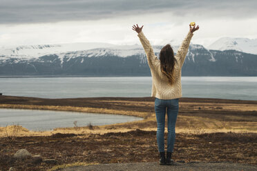 Iceland, woman standing at lakeside with raised arms - KKAF01059