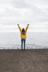 Iceland, woman standing at the sea with raised arms - KKAF01062