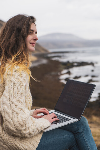 Island, Frau mit Laptop an der Küste, lizenzfreies Stockfoto