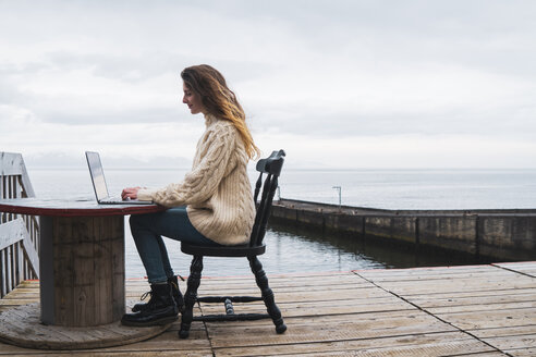 Island, Frau benutzt Laptop am Meer - KKAF01074