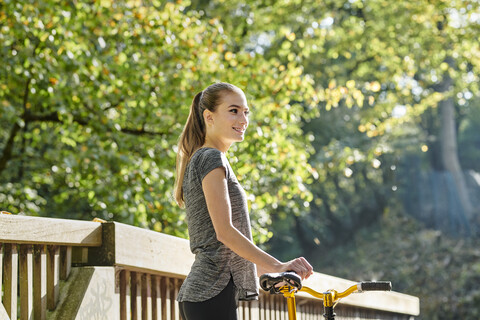 Lächelnde sportliche junge Frau mit Fahrrad in einem Wald, lizenzfreies Stockfoto