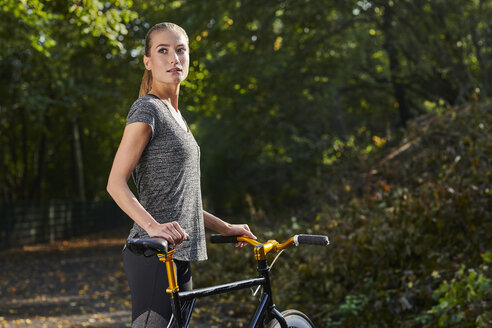 Portrait of sportive young woman with bicycle in a forest - MMIF00077