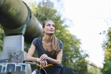 Porträt einer sportlichen jungen Frau mit Fahrrad, die zur Seite schaut - MMIF00078