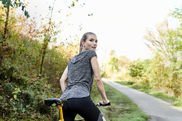 Rückansicht einer sportlichen jungen Frau mit Fahrrad in einem Park - MMIF00079