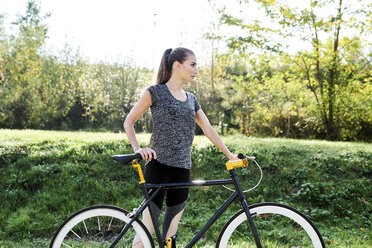 Sportive young woman with bicycle in nature - MMIF00081