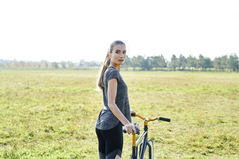 Sportliche junge Frau mit Fahrrad auf einer Wiese, lizenzfreies Stockfoto