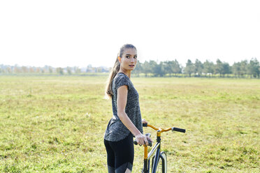 Sportliche junge Frau mit Fahrrad auf einer Wiese - MMIF00084