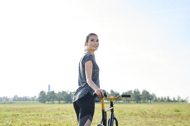 Lächelnde sportliche junge Frau mit Fahrrad auf einer Wiese - MMIF00085