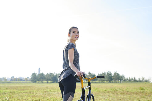 Smiling sportive young woman with bicycle on a meadow - MMIF00085