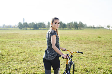 Sportliche junge Frau mit Fahrrad auf einer Wiese - MMIF00086