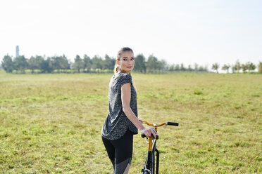 Sportliche junge Frau mit Fahrrad auf einer Wiese - MMIF00087