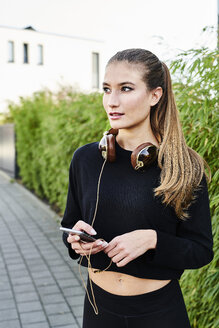 Sportive young woman with headphones and cell phone outdoors - MMIF00103