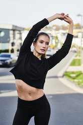 Sportliche junge Frau beim Stretching auf einer Straße in der Stadt - MMIF00107