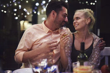 Couple sitting at table, holding wine glasses, face to face, smiling - ISF05788