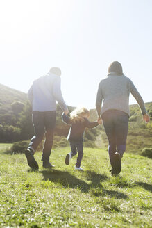 Rückansicht eines erwachsenen Paares und einer Tochter, die auf einem Feld spazieren gehen - ISF05789