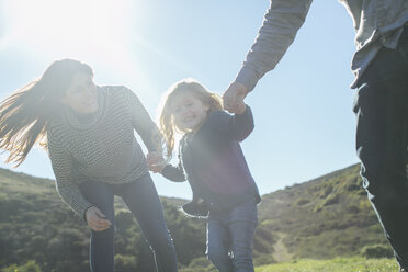 Sunlit portrait of mid adult couple and daughter holding hands in field - ISF05790