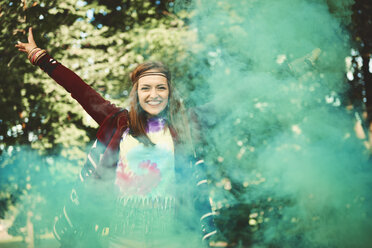 Young boho woman dancing with green smoke flare at festival - ISF05834