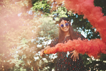 Young boho woman dancing with red smoke flare at festival - ISF05855