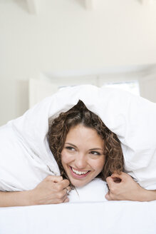 Frau auf dem Bett liegend unter der Bettdecke lächelnd - ISF05905