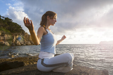 Woman sitting on rocks by sea meditating, Palma de Mallorca, Islas Baleares, Spain, Europe - ISF05909