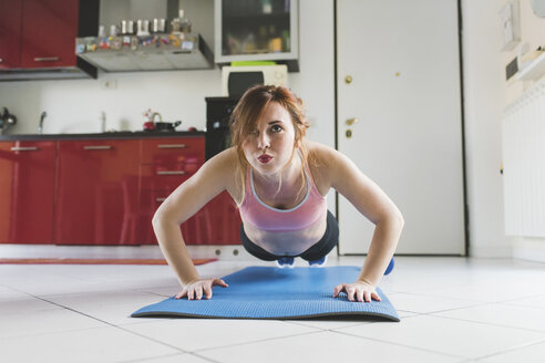 Portrait of young woman doing push ups on kitchen floor - ISF05913