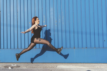 Woman in front of blue wall jumping in mid air - ISF05915