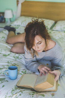 Young woman reclining on bed reading a book - ISF05929