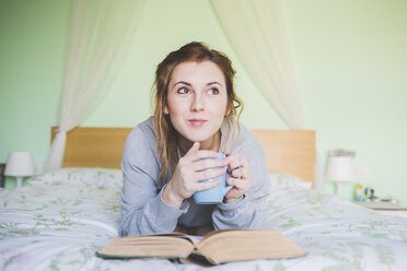 Young woman lying on bed holding coffee cup and looking up - ISF05930