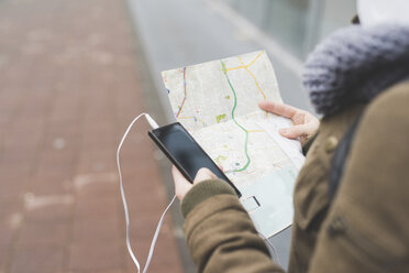 Over shoulder view of female backpacker with smartphone looking at map on city sidewalk - ISF05940