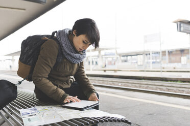 Weiblicher Rucksacktourist mit Blick auf Karte und digitales Tablet auf dem Bahnsteig - ISF05944