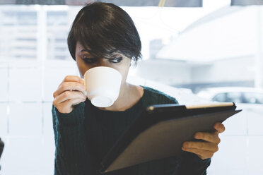 Frau im Café schaut auf ein digitales Tablet und trinkt Kaffee - ISF05952