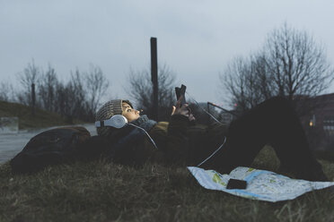 Weibliche Rucksacktouristin liegt nachts im Stadtpark und schaut auf ihr Smartphone - ISF05955