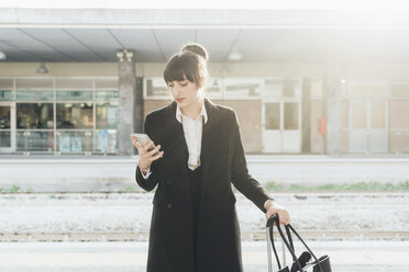 Businesswoman using mobile phone in train station, Milan, Italy - ISF05957