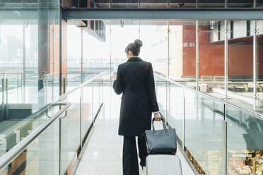 Businesswoman using mobile and pulling trolley luggage, Milan, Italy - ISF05961