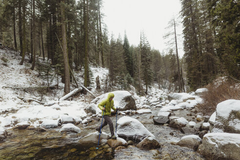 Männlicher Wanderer, der über Flussfelsen im verschneiten Sequoia National Park, Kalifornien, USA, schreitet - ISF06014