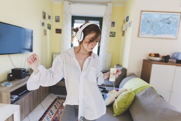 Young woman in sitting room dancing to smartphone music on headphones - ISF06024