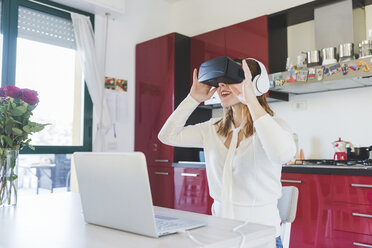 Junge Frau am Küchentisch schaut durch ein Virtual-Reality-Headset - ISF06031