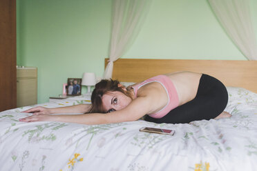 Junge Frau übt Yoga und beugt sich auf dem Bett vor - ISF06034