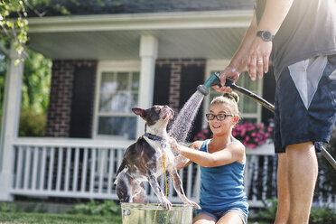 Vater und Tochter waschen Hund mit Schlauch - ISF06054