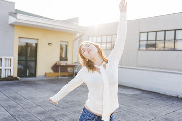 Beautiful young woman dancing on sunlit roof terrace with eyes closed - ISF06056