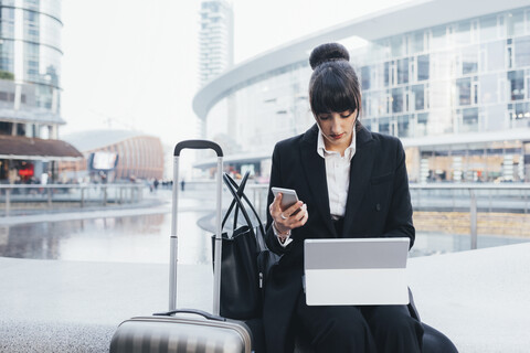 Geschäftsfrau mit Gepäckwagen, die ein Mobiltelefon und ein digitales Tablet benutzt, Mailand, Italien, lizenzfreies Stockfoto