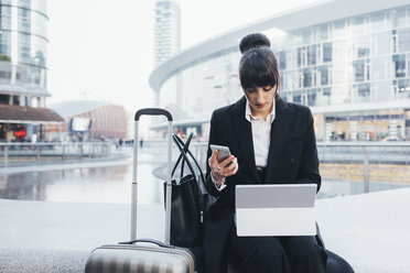 Geschäftsfrau mit Gepäckwagen, die ein Mobiltelefon und ein digitales Tablet benutzt, Mailand, Italien - ISF06102