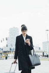 Businesswoman using mobile and pulling trolley luggage, Milan, Italy - ISF06107