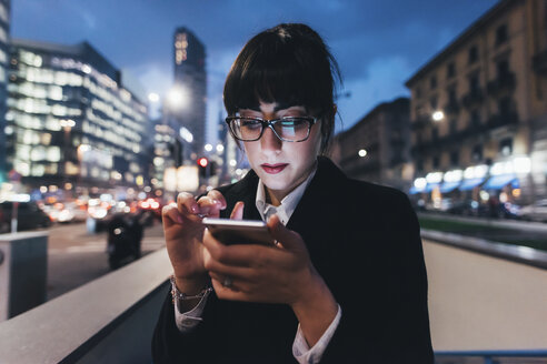 Businesswoman using mobile phone by wall on busy road, Milan, Italy - ISF06112