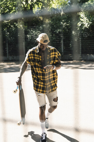 Cooler junger Mann im Skatepark, der sein Smartphone benutzt, lizenzfreies Stockfoto