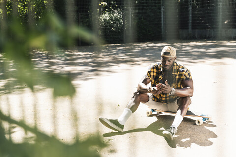 Cooler junger Mann im Skatepark, der sein Smartphone benutzt, lizenzfreies Stockfoto