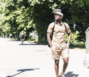 Young man walking in the city, carrying guitar case - UUF13859