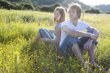 Romantic young couple sitting back to back in wildflower field, Majorca, Spain - CUF13195