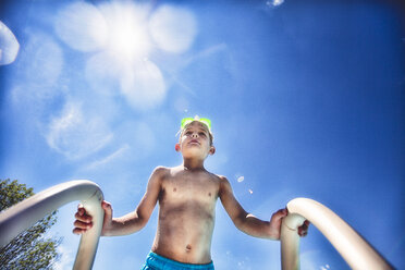 Low angle view of boy on swimming pool ladder against blue sky - ISF06120