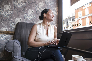 Geschäftsfrau in einer Kaffeebar, die mit ihrem Laptop durch ein Fenster schaut - ISF06155